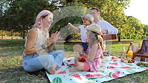 A family has fun during a picnic, mother plays with her daughter and father plays the guitar