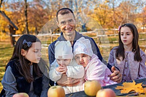 family has picnic in autumn city park, father and daughters, children and parent sitting together at the table, with apples and