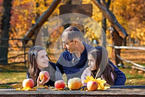 family has picnic in autumn city park, father and two daughters, children and parent sitting together at the table, with apples