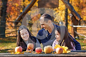 family has picnic in autumn city park, father and two daughters, children and parent sitting together at the table, with apples