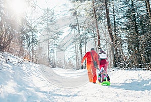 Family have active walk in winter forest. Mother and father pull