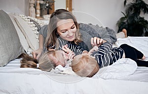 Family having fun at home. Happy young mother playing with children in bedroom. Brother and sister embracing on the bed. Sunny hol