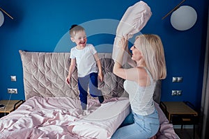 Family having fun together at the weekend together.Mother and child on bed. blonde mom and baby boy playing pillow fight
