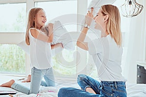 Family having funny pillow fight on bed. Beautiful mom with her little cute daughter spending free time together