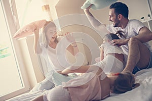 Family having funny pillow fight on bed.