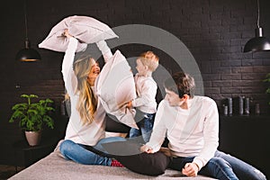 Family having funny pillow fight on bed. Parents spending free time with their son. Young family being playful at home