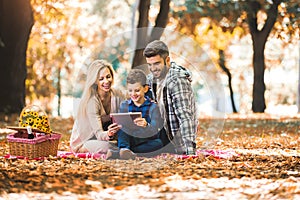 Family having picnic in autumn park, using digital tablet