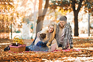 Family having picnic in autumn park, using digital tablet