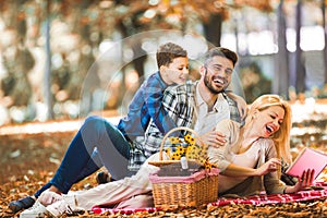 Family having picnic in autumn park, using digital tablet