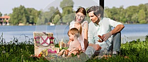 Family having picnic at lake sitting on meadow