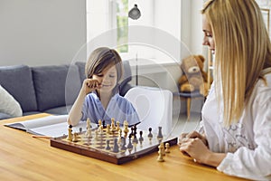 Family hobbies. Young mother playing chess with son at home. Little boy engaged in board game with his parent in room