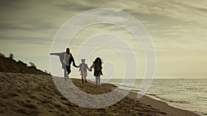 Family hold hands beach by sunset sea. Mom dad child running sand on holiday.