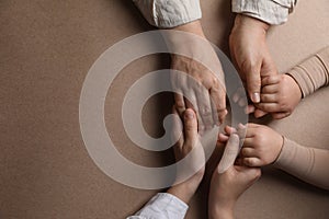 Family holding hands together on brown background, top view. Space for text