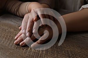 Family holding hands together at wooden table, closeup