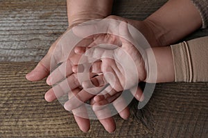 Family holding hands together at wooden table, top view