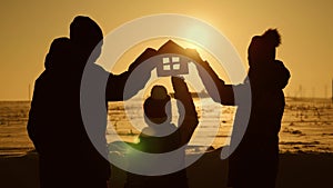 The family holds a paper house at sunset, dreaming of their own home. Silhouette of a paper house in hands at sunset in