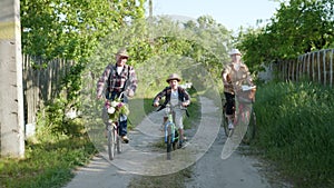 Family holiday, male kid in sun hat with their merry grandmother and grandfather ride bicycles during outdoor activities