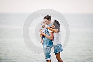 Family holiday in nature. Three, Mom, Dad, daughter one year standing with backs on cliff overlooking sea. man holding hild in