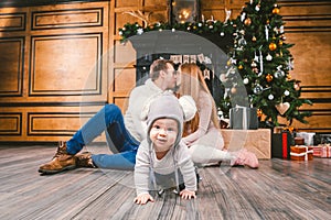 Family holiday New Year and Christmas. Young caucasian family mom dad son 1 year sit wooden floor near fireplace christmas tree on