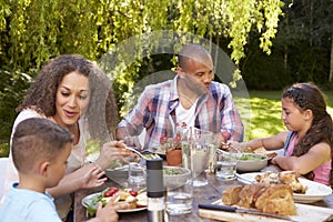 Family At Home Eating Outdoor Meal In Garden Together