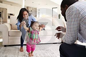 Family At Home Encouraging Baby Daughter To Take First Steps