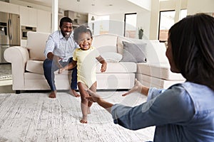 Family At Home Encouraging Baby Daughter To Take First Steps