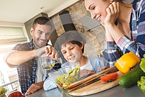 Family at home leaning on table in kitchen together looking happy at father dressing salad with oil close-up