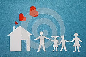 Family and home love concept. Paper house and family on blue textured background. Dad, mom, daughter and son hold hands.