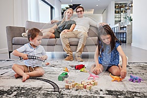 Family home, parents and children with toys on carpet in living room for holiday with mother and father love, care and