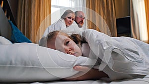 A family in the hotel room - a girl sleeping in bed - her mom and dad looking at her