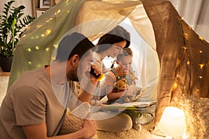 Happy family reading book in kids tent at home