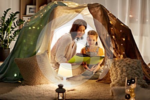 Happy family reading book in kids tent at home