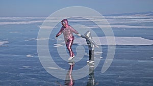 Family is ice skating at day. Girls to ride figure ice skates in nature. Mother and daughter riding together on ice in