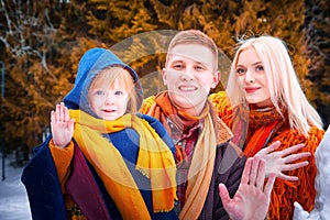 Family including father, mother, little daughter in yellow, red and brown dress on a walk in winter. A man and woman