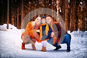 Family including father, mother, little daughter in yellow, red and brown dress on a walk in winter. A man and woman