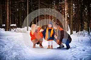 Family including father, mother, little daughter in yellow, red and brown dress on a walk in winter. A man and woman