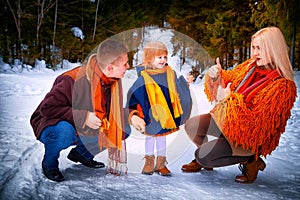 Family including father, mother, little daughter in yellow, red and brown dress on a walk in winter. A man and woman