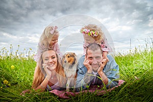 A family including two young parents and daughters on a walk in a meadow with grass and flowers. Dad, mom, girls relaxing and