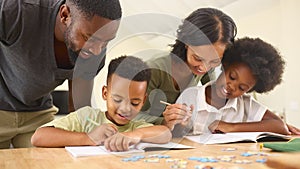 Family Indoors At Home With Parents Helping Children With Homework Sitting At Table photo