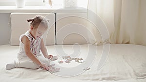 Family, infant, education, mental development concepts - One cute little three-year girl make puzzles on white bed in