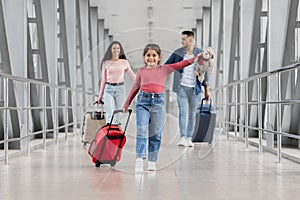 Family Journey. Little Girl Carrying Suitcase While Walking With Parents At Airport