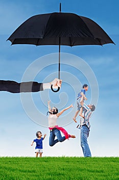 Family jumping under umbrella on the meadow