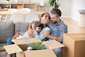 Family with kid embracing on sofa moving in new home