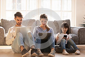 Family with kid sitting on floor at home using devices photo