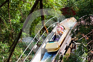 Family with kids on roller coaster in amusement theme park. Children riding high speed water slide attraction in entertainment fun