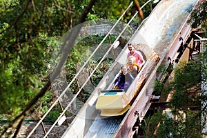 Family with kids on roller coaster in amusement theme park. Children riding high speed water slide attraction in entertainment fun