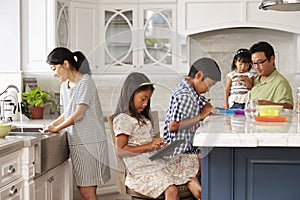 Family In Kitchen Doing Chores And Using Digital Devices