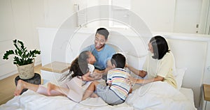 Family, laughing for tickle and parents with children on bed in home together for weekend bonding. Love, smile or happy