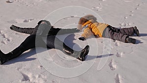 Family laying in snow making snow angels. Mother and child lying on snow.