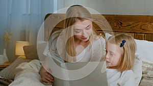 Family learning concept. Caucasian mother help little small cute daughter preschool child girl baby reading book in bed